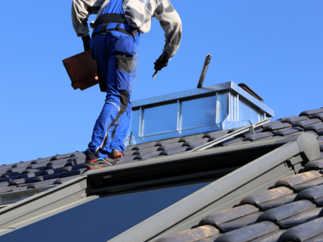 Roofer working beside a metal flue on a tiled roof
