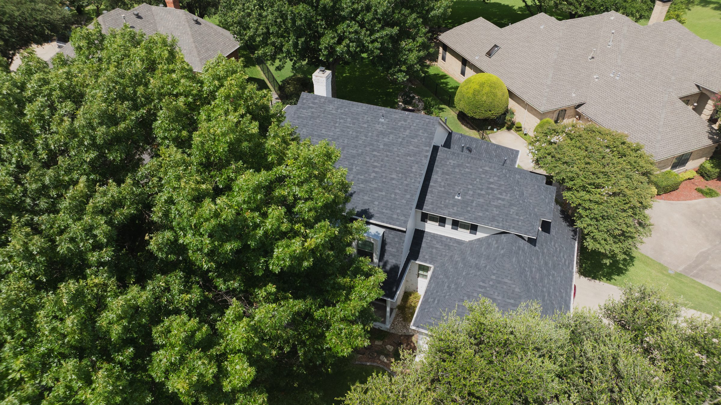 Aerial view of a dark shingle roof on a North Texas home, surrounded by trees